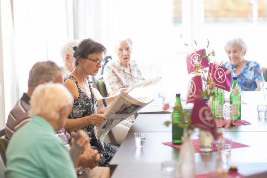 Eine Betreuerin liest Seniorinnen und Senioren aus der Zeitung vor