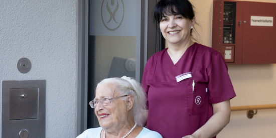 Mitarbeiterin schiebt Bewohnerin im Rollstuhl